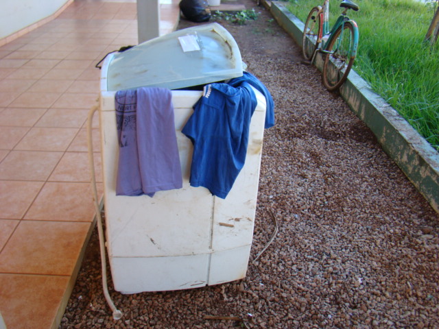 Corpo de bombeiro é acionado para combater incêndio e encontra máquina de lavar roupas, em matagal.
